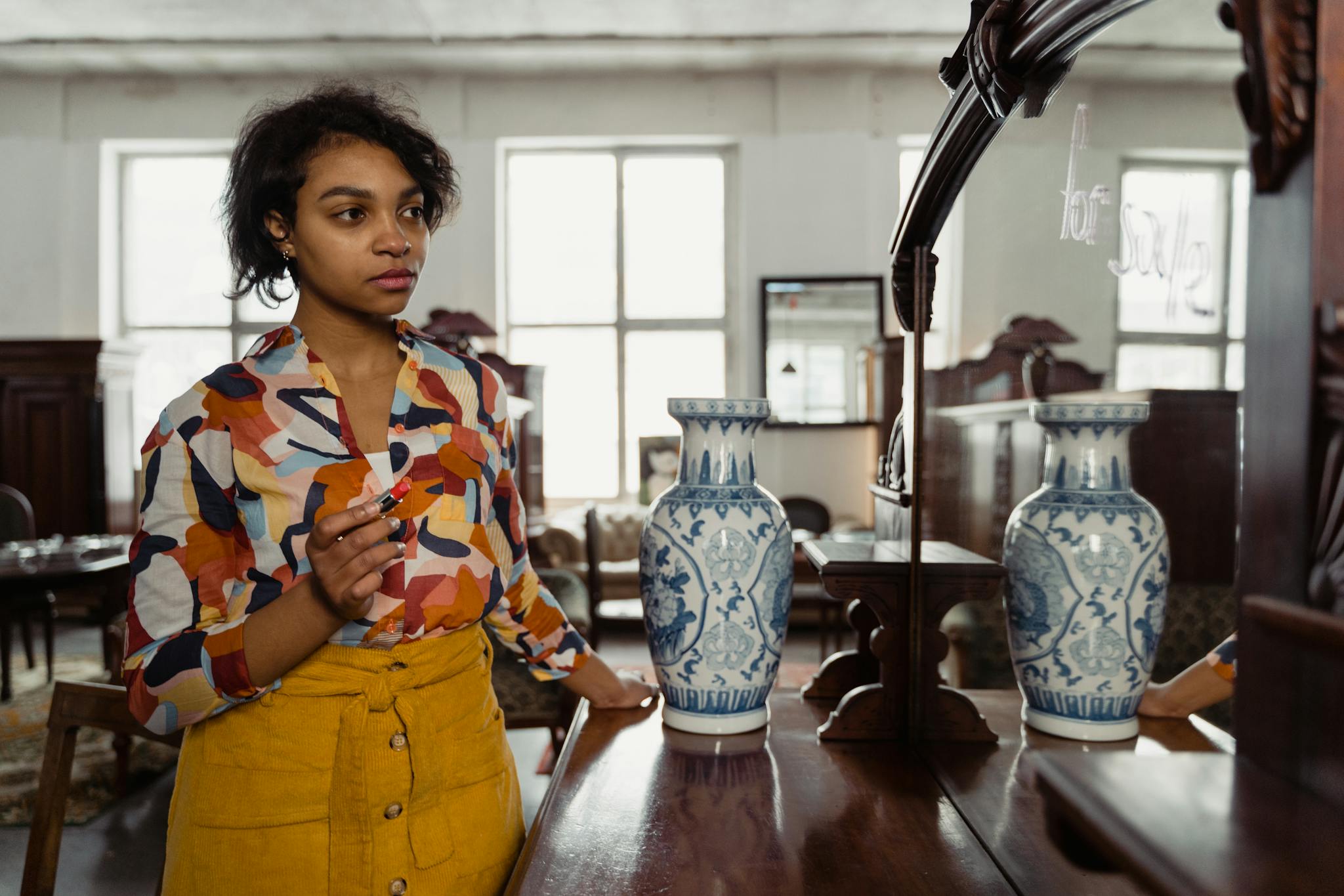 Woman in a colorful shirt admiring her reflection in a mirror with vases, in an antique shop setting.